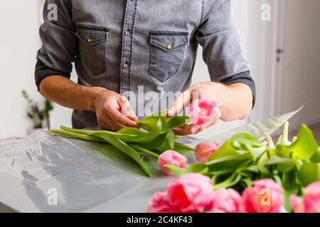 Blumen Lieferladen. Florist, der Ordnung schafft, Frühlingsstrauß macht. Männlich machen Bouquet mit Tulpen Stockfoto