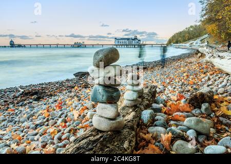 Strandabschnitt an der Ostseeküste. Steinige Küste bei Sonnenuntergang mit Wolken auf der Insel Rügen. Stein Männer auf einem alten Baumstamm und Laub aut Stockfoto