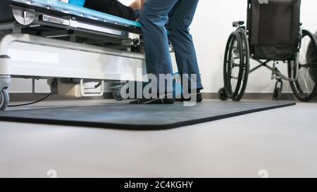 Physiotherapeut, der mit behinderten Menschen im Rollstuhl auf einem Therapietisch trainiert. Stockfoto