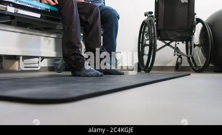 Physiotherapeut, der mit behinderten Menschen im Rollstuhl auf einem Therapietisch trainiert. Stockfoto