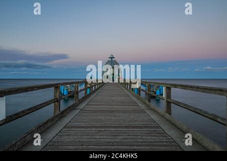 Holzsteg mit Geländer entlang der Küste und Sprungglocke am Ende. Pier an der Ostsee am Abend. Abendhorizont mit Wolken und Ca Stockfoto