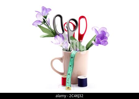 Schneiderschere oder Schneiderschere und Maßband in einer Kaffeetasse mit Blumen auf weiß isoliert gefüllt Stockfoto