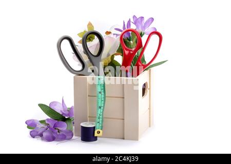 Schneiderschere oder Schneiderschere und Maßband in einer Holzkiste mit Blumen isoliert auf gefüllt Stockfoto