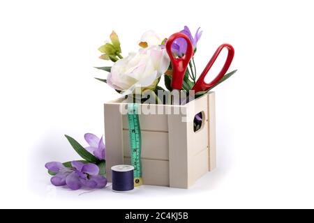 Schneiderschere oder Schneiderschere und Maßband in einer Holzkiste mit Blumen isoliert auf gefüllt Stockfoto