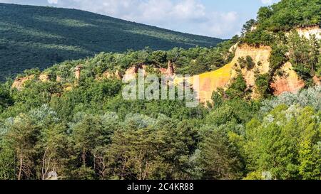 Schöne rote Hügel bedeckt von Bäumen der Colorado Provence in Rustrel, Frankreich Stockfoto