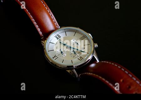 Schöne Luxus-Armbanduhr mit blauen Zeigern und braunem Lederarmband auf schwarzem Hintergrund Stockfoto