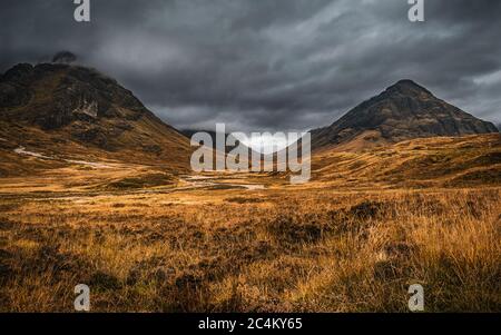 Herbstlandschaft in Glen Coe, Schottland, mit dunklen Wolken, die über den Gipfeln von Buachaille Etive Beag und Aonach Eagach hängen. Stockfoto