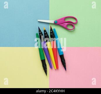 5 bunte Markierstifte und eine Kinderschere auf bunten Quadraten aus Baupapier Stockfoto