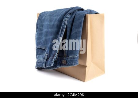 Eine Jeans in Denim-Blau, die über einer braunen Einkaufstasche aus Papier hängt, isoliert auf Weiß Stockfoto