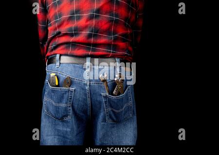 Ein Mann in blauer Denim-Jeans und einem roten karierten Hemd mit Mechanikwerkzeugen auf Schwarz Stockfoto