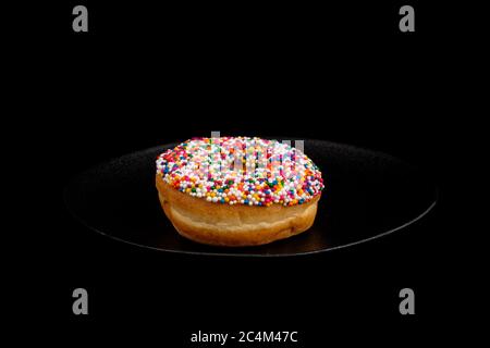 Ein Donut mit Streuseln auf einer schwarzen Platte isoliert auf schwarz Stockfoto