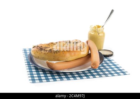 Eine große deutsche Brezel und zwei österreichische Würstchen auf einem blauen Teller und ein Glas französischen Senf isoliert auf weiß Stockfoto