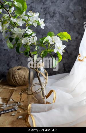 Moderne Einrichtung im rustikalen Stil. Wohnkultur, Vase mit blühenden Apfelzweig auf Holztisch in der Nähe des Fensters mit Vorhang. Konzept von Komfort und Zuhause Stockfoto