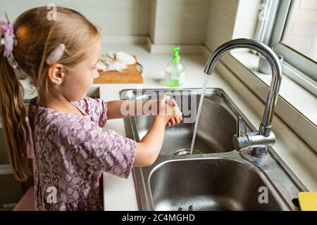 Ein nettes kleines Mädchen mit blonden Haaren, die Hände in der Küche waschen. Schutz vor Infektionen und Viren während der Coronavirus covid-19 Pandemie. Stockfoto