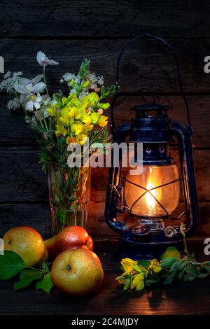 Stillleben mit Kerosin Lampe, Bouquet von wilden Blumen und reifen Birnenfrucht. Auf dem Holztisch ist die Lampe beleuchtet, die Früchte und Blumen beleuchtet Stockfoto