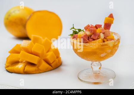 Glas gefüllt mit Fruchtcocktail mit einer halben Mango daneben Stockfoto