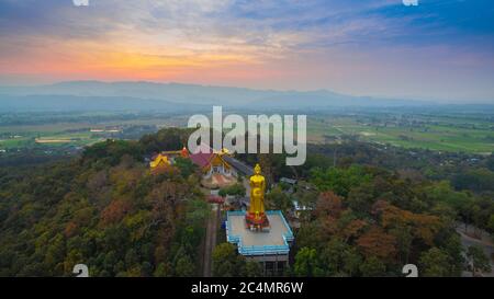 Luftaufnahmen der golden Big Buddha Statue stehend auf einem Hügel im Sonnenuntergang am Wat Phra That Jom Wae in Chiang Rai Thailand Stockfoto