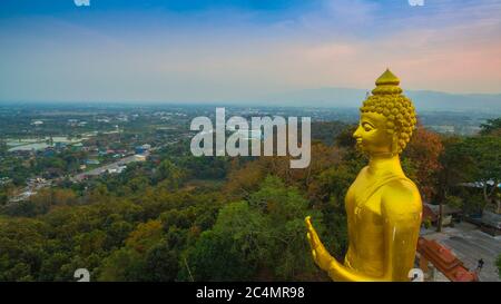 Luftaufnahmen der golden Big Buddha Statue stehend auf einem Hügel im Sonnenuntergang am Wat Phra That Jom Wae in Chiang Rai Thailand Stockfoto