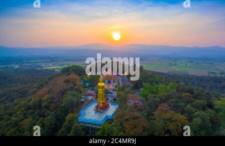 Luftaufnahmen der golden Big Buddha Statue stehend auf einem Hügel im Sonnenuntergang am Wat Phra That Jom Wae in Chiang Rai Thailand Stockfoto