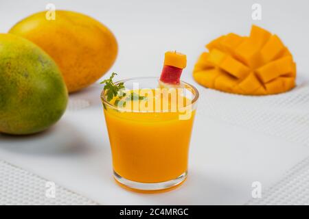 Ein Glas gefüllt mit Mangosaft im Vordergrund und im Hintergrund zwei ganze Mangos auf der einen Seite und eine halbe Mango auf der anderen Seite Stockfoto