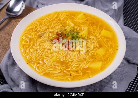 Weißer Teller mit gelber Suppe mit Nudeln serviert und mit roten und grünen Chilischoten in der Mitte verziert Stockfoto