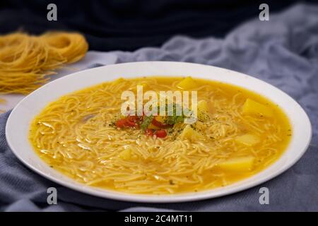 Weißer Teller mit gelber Suppe mit Nudeln serviert und mit roten und grünen Chilischoten in der Mitte verziert Stockfoto