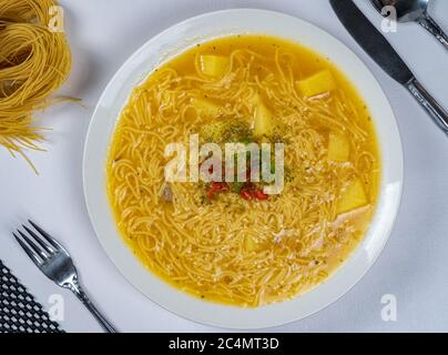 Draufsicht auf einen weißen Teller mit gelber Suppe mit Nudeln serviert und mit roten und grünen Chilischoten in der Mitte dekoriert Stockfoto