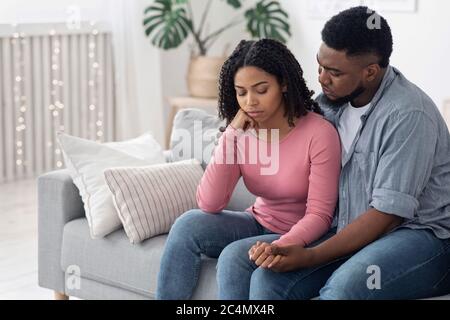 Fürsorglicher Afro Mann Tröstet Seine Depressive Frau Zu Hause, Umarmt Und Unterstützt Stockfoto