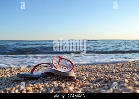 Sandalen am Strand. Sommerurlaubskonzept, Orange Flip Flops an einem Sandstrand. Stylische Flip Flops auf Sand am Meer, Stockfoto