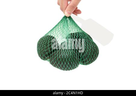 Weibliche Hand hält eine frische Bio-hass Avocados in einem grünen Mesh-Tasche mit einem grauen Tag isoliert auf weiß. Gesundes Lebensmittelkonzept. Stockfoto