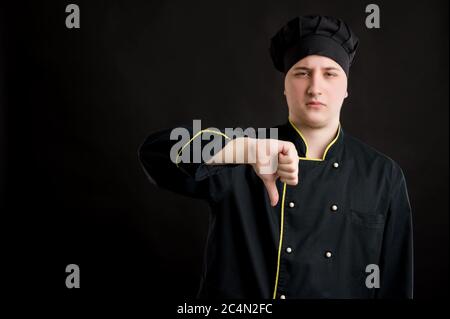 Portrait von jungen Mann in einem schwarzen Koch Anzug gekleidet zeigt Abneigung posiert auf einem schwarzen isolierten Hintergrund mit Kopie Raum Werbefläche Stockfoto