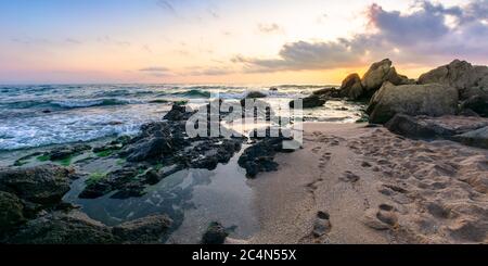 Idyllischer Sonnenuntergang am Meer. Wellen krachende Felsen am Sandstrand. Wunderschöne Wolkenlandschaft über dem Horizont Stockfoto