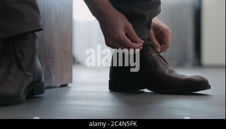 Junger Mann schnürt seine braunen Leder-Chukka-Stiefel innen Stockfoto