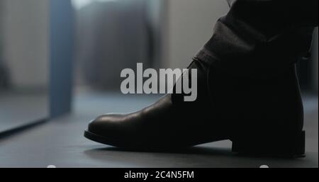 Junger Mann schnürt seine braunen Leder-Chukka-Stiefel innen Stockfoto