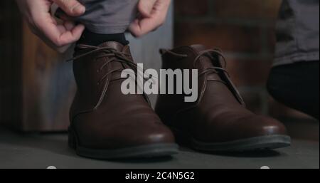 Junger Mann schnürt seine braunen Leder-Chukka-Stiefel innen Stockfoto