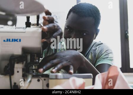 Politische Flüchtlinge und afrikanische Einwanderer arbeiten an der Schneiderei der gemeinnützigen Vereinigung im Süden Italiens, Neapel. Stockfoto