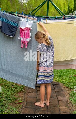 Townsville, Queensland, Australien - 2020. Juni: Junge blonde Kaukasierin, die die Wäsche an der Wäscheleine hängt Stockfoto