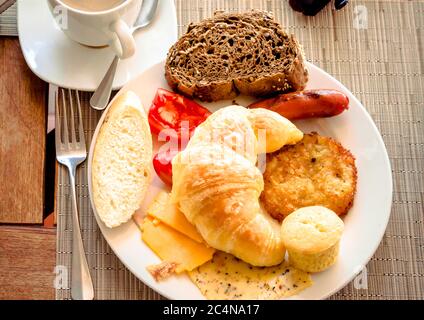 Frühstück im Café mit einer Tasse Kaffee und Croissant, Brot, Käse, Tomaten auf dem Teller. Stockfoto