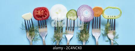 Scheiben Pfeffer, Zwiebel, Gurke, Karotte, Tomaten und Knoblauch auf Gabeln hinter einem blauen Hintergrund Stockfoto