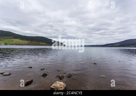 Fluss, der ruhig mit hohen Bergen umgeben ist, die unter dem glitzern wolkiger Himmel Stockfoto