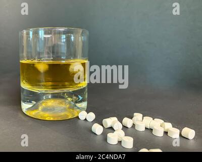 Ein Glas Whisky mit Eis und vielen weißen Pillen auf grauem Hintergrund. Suizid-Konzept mit Tabletten und Alkohol. Bild auf Lager. Stockfoto