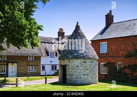 Das Old Village Lock Up Gefängnis oder Blind House umgeben von Hütten auf dem Grün in Harrold, Bedfordshire, Großbritannien Stockfoto