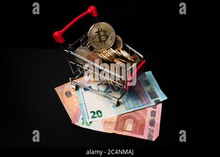 Miniatur-Warenkorb gefüllt mit Euro-Münzen und einem Bitcoin auf der Oberseite auf Papiergeld mit schwarzem Hintergrund platziert. Geld verdienen Krypto Währung. Stockfoto