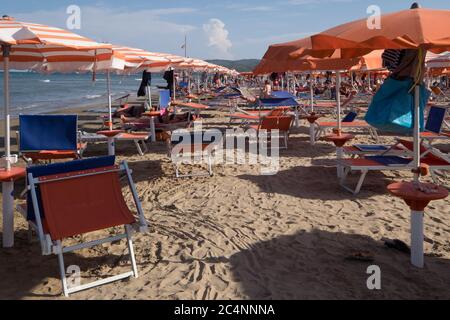 Sandstrand mit orangefarbenen Sonnenschirmen, Liegen und Liegen mit Sonnenbaden Menschen in Italien Stockfoto