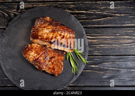 Ein saftiges Stück gebratenem Fleisch liegt auf einer Steinplatte vor einem schwarzen Holztisch. Grad der Röstung gut getan. Essen Konzept mit Kopie Raum Stockfoto