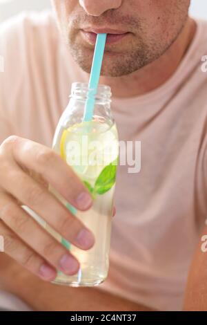 Man trinkt Limonade durch einen Strohhalm aus der Glasflasche. Abgeschnitten. Stockfoto