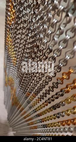 Selektive Konzentration auf silberne und goldfarbene Ketten-Textur. Ungewöhnlicher Vorhang aus verzierten Metallkettengliedern in Reihen hängen Stockfoto