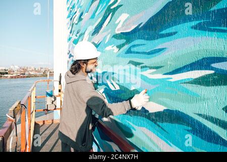 Graffiti-Künstler malt eine weiße Wand in großer Höhe in Wellen. Graffiti nach allen Regeln erlaubt Stockfoto