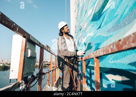 Graffiti-Künstler malt eine weiße Wand in großer Höhe in Wellen. Graffiti nach allen Regeln erlaubt Stockfoto