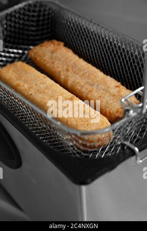 Fischfinger in einem Korb, der in einer elektrischen Fritteuse gegart wird. Fast Food-Konzept Stockfoto